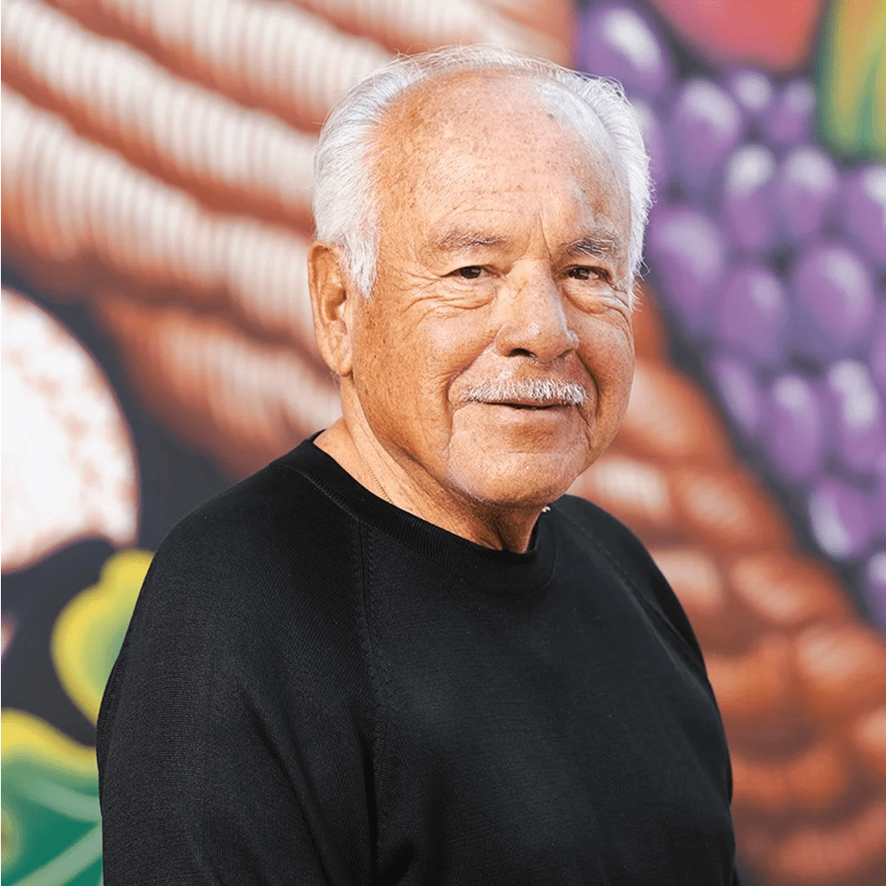 An elderly man with white hair and a black shirt smiling gently.
