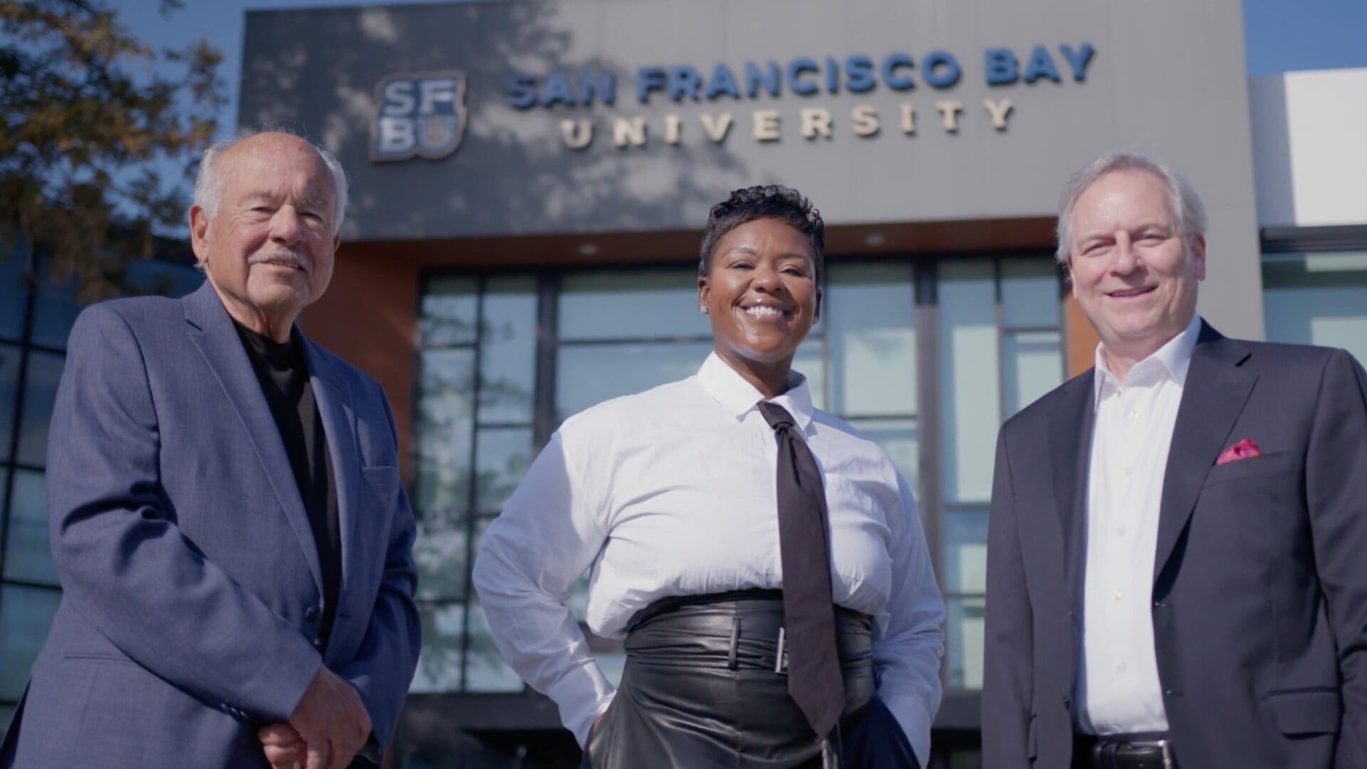 Three professionals standing outside a university building, smiling.