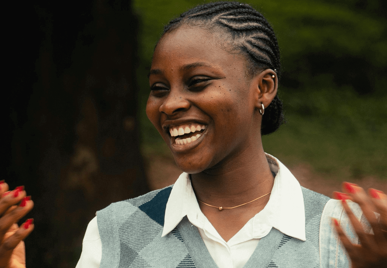 A woman with braided hair smiling outdoors.