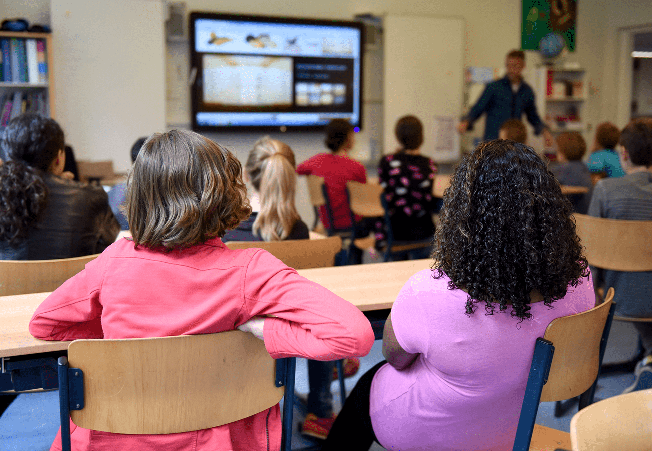 Children attentively watching a lesson on a screen in a classroom.