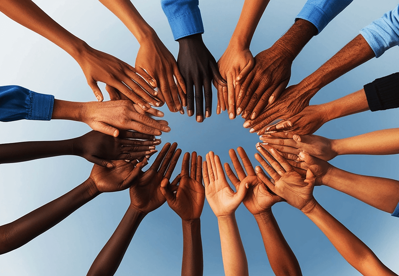 Diverse hands joined together forming a circle against the blue sky.