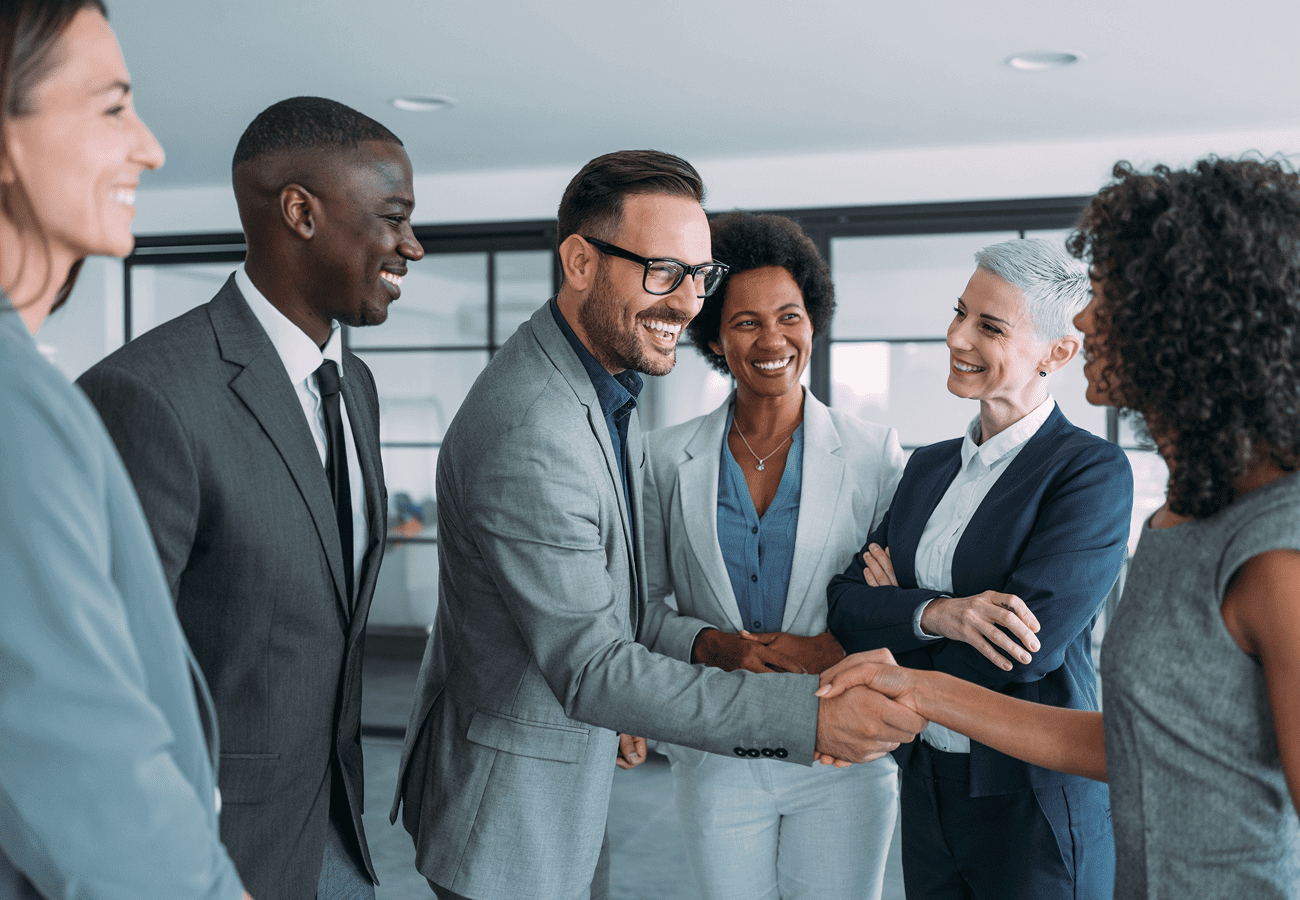 Four professionals smiling and shaking hands in an office.