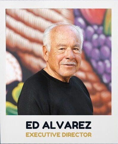 Older man smiling with colorful background mural.