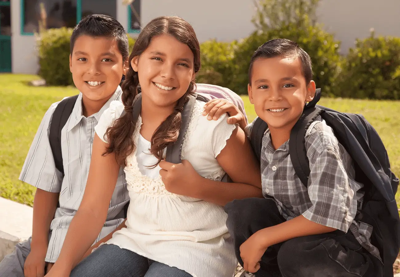 Three smiling children with backpacks outdoors